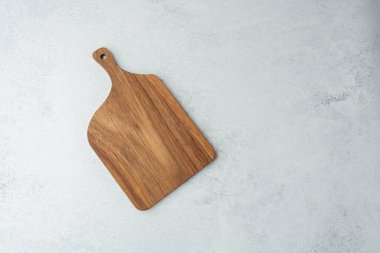 Tahta kesme tahtası açık gri bir tezgahın üzerinde asgari dekorasyonla duruyor..