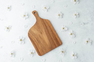 Yumuşak bir yüzeyde dağınık beyaz çiçeklerin arasında bir tahta kesme tahtası duruyor..