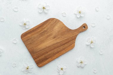 Küçük beyaz çiçeklerle çevrili açık bir yüzeyde tahta kesme tahtası sergilenir..