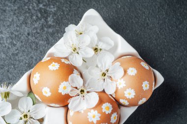 Karanlık bir yüzeyde beyaz çiçeklerle çevrili güzel dekore edilmiş üç yumurta..