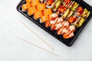 Yakınlarda yemek çubukları olan siyah bir tepside renkli suşi çeşitleri sergileniyor.