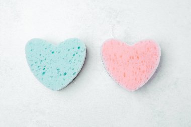 Yumuşak mavi ve pembe renkte iki kalp şeklinde sünger açık bir yüzeyde dinleniyor..