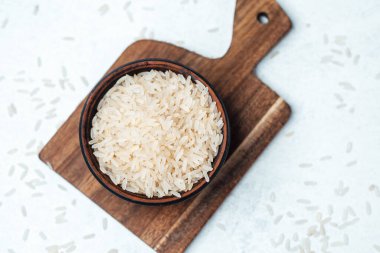 Seramik bir kase, dağınık taneli bir kesme tahtasının üzerinde pişmemiş pirinç tutar..