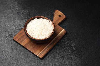 Pişmemiş beyaz pirinç, ahşap bir kesme tahtasındaki kahverengi bir kaseye düzgünce yerleştirilir..