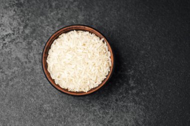 Taze pişmemiş beyaz pirinç, koyu bir yüzeyde, kırsal bir kasede oturur..