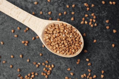 Karabuğday tohumları bir tahta kaşıkta oturur ve ek tohumlar koyu bir yüzeye yayılır..