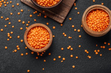 Parlak turuncu mercimekler ahşap kaselerde koyu renkli bir yüzey üzerinde sergilenir..