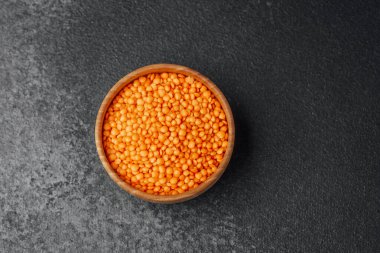 Koyu bir tezgahın üzerinde içi turuncu mercimek dolu küçük tahta bir kase..