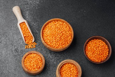 Koyu bir yüzeye yerleştirilmiş parlak turuncu mercimeklerle dolu dört tahta kase..