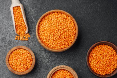 Parlak turuncu mercimekler, çeşitli ahşap kaselerde koyu renkli taş arka planda sergilenir..