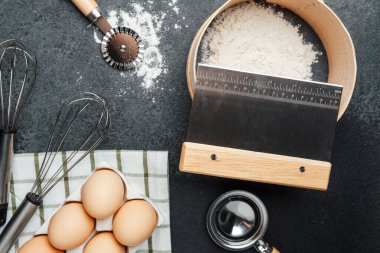 Hazırlık için çeşitli pişirme araçları ve malzemeler koyu bir tezgahta düzenlenir..