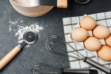 Yumurta, un ve mutfak aletlerinden oluşan bir koleksiyon pişirmek için karanlık bir yüzeye yerleştirilir..