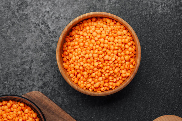 Крупный план деревянной чаши, наполненной яркими апельсиновыми чечевицами на темном камне.