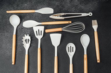 Koyu bir tezgahta kaşık ve spatula da dahil olmak üzere çeşitli mutfak araçları sergilenmektedir..