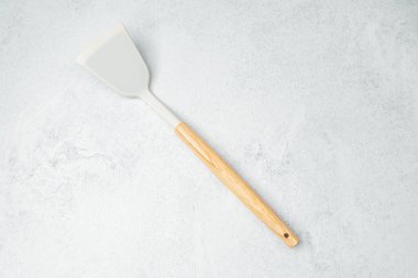Pürüzsüz bir yüzeyi ve tahta sapı olan bir mutfak spatulası gri arka planda yatar..