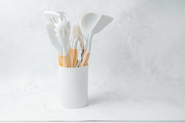 Çeşitli mutfak aletleri, arka planda beyaz bir klasörde dikey durur..