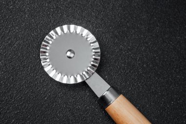 Dekoratif bir fırın çarkı hamurun yanında, koyu bir tezgahın üzerinde duruyor..