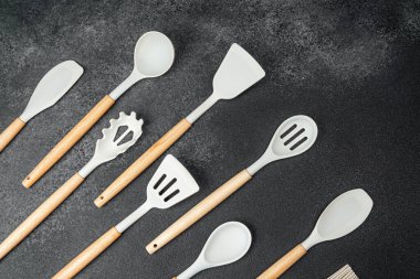 Silikon ve ahşaptan yapılmış çeşitli mutfak aletleri karanlık bir tezgahta sergileniyor..