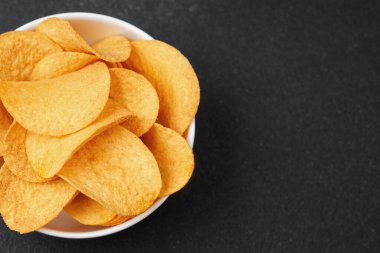 Altın patates cipsi dolu bir kase karanlık bir tezgahın üzerinde, paylaşmak için mükemmel..
