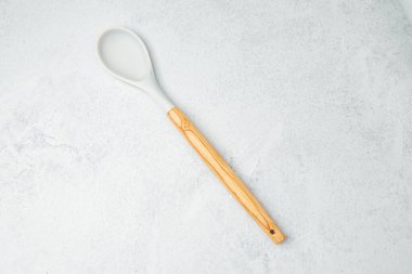 Tek bir tahta kaşık, aşçılık görevleri için hazır, pürüzsüz, gri bir yüzeye uzanıyor..