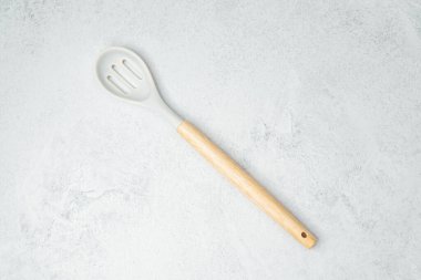 Ahşap bir yemek kaşığı pürüzsüz gri bir yüzeye uzanır, yemek hazırlığı için hazırdır..
