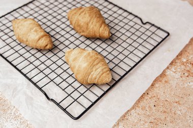 Taze kruvasanlar parşömen ve taş zeminde tel askıda soğuyor.