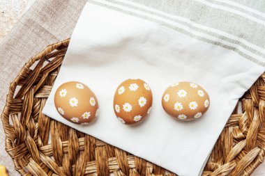 Hasır sepetinde papatya çiçekleri olan el yapımı Paskalya yumurtaları. Şenlikli kutlama için kırsal bahar kompozisyonu