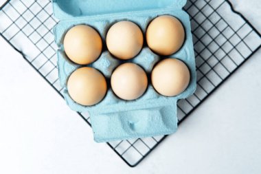 Açık mavi arka planda mavi bir karton kutuda kahverengi tavuk yumurtası.