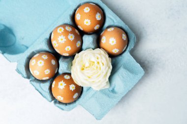 El boyaması Paskalya yumurtaları, papatya desenli beyaz güllü mavi bir karton. Işık arkaplanındaki Paskalya kompozisyonu