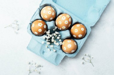Papatya motifli el yapımı Paskalya yumurtaları ve mavi kartonda çingene çiçekleri. Yumuşak bahar tatili