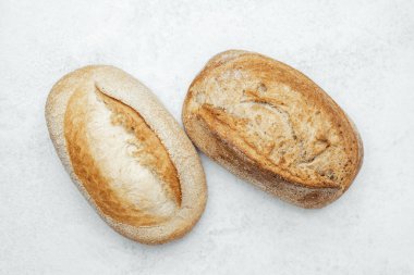 Gri bir yüzey üzerinde farklı kabukları ve dokuları olan iki sade ekmek somunu..