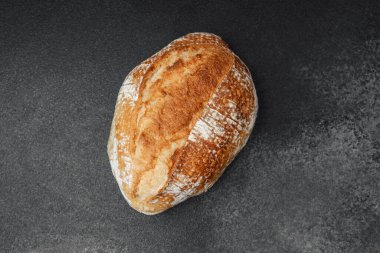 Kabuklu, altın rengi bir somun ekmek dilimlenmeye hazır, koyu renkli bir yüzeyde oturur..