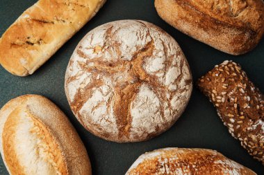 Koyu bir arkaplanda gösterilen çeşitli ekmekler dokularını renklendiriyor.