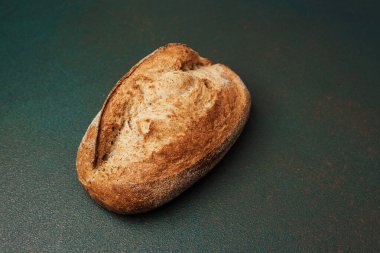 Bir somun kabuklu ekmek, karanlık bir yüzeyde tek başına oturur ve altın bir kabuk sergiler..