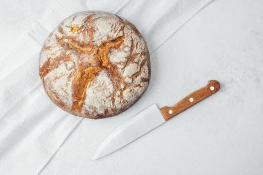 Kabuklu, yuvarlak bir ekmek, hafif bir yüzeyde keskin bir bıçağın yanında oturur..