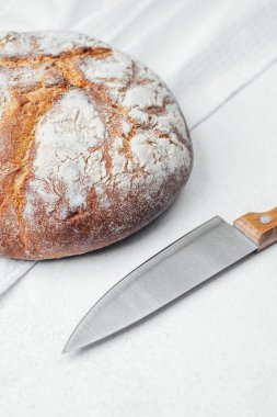 Yuvarlak bir somun ekmek, sade bir mutfak yüzeyinde bıçağın yanında oturur..