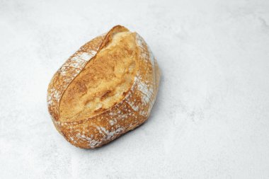 Kabuklu bir zanaatkar ekmek yumuşak gri bir zeminde oturur, altın kabuğunu ön plana çıkarır..