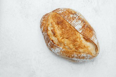 Kırsal bir ekmek somunu temiz bir yüzeye uzanır ve altın kabuğunu sergiler..