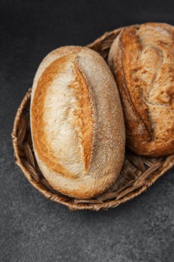 İki somun kabuklu ekmek desenli, koyu bir tezgahın üzerinde bir sepette dinleniyor..