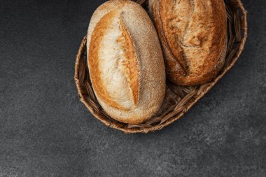 İki altın kahverengi ekmek kırsal bir sepetin içinde dinleniyor.