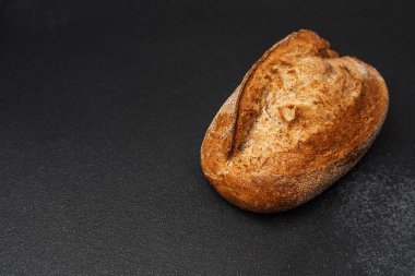 Yuvarlak bir ekmek somunu karanlık bir yüzeyde oturur ve kabuğunu gösterir..