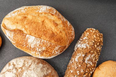 Koyu bir tezgahta çeşitli ekmekler sergileniyor, dokuları vurgulanıyor..