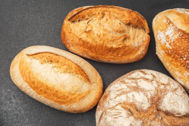 Koyu bir yüzeyde dört çeşit zanaatkar ekmek sergilenir, taze pişmiş gibi görünür..