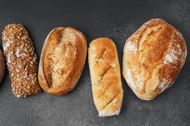 Farklı şekillerde ve renklerde sanatsal ekmek somunları karanlık bir yüzeye düzgün bir şekilde dizilmiştir..