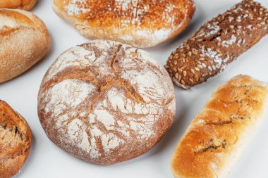 Beyaz bir yüzeye düzgün bir şekilde yerleştirilmiş çeşitli taze ekmek türleri.