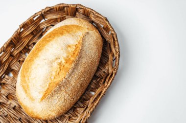 Bir somun kabuklu ekmek sade bir arka planda sade bir hasır sepette duruyor..