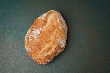 Kır mayalı ekmek, karanlık bir tezgahın üzerinde duruyor ve sanatsal dokusunu sergiliyor..