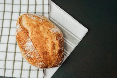 Ekmek, kabuklu dokusunu gösteren kareli bir mutfak havlusuna dayanır..