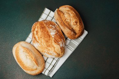 Konforlu bir mutfaktaki kareli kumaş üzerinde sergilenen üç çeşit zanaatkar ekmek..