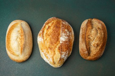 Koyu yeşil bir tezgahta üç çeşit taze ekmek sergilenir..